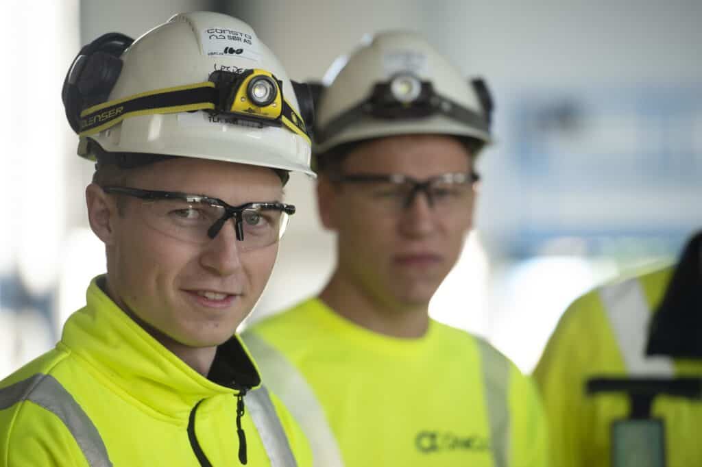 To OneCo-ansatte ser på kameraet, iført hjelmer og briller.