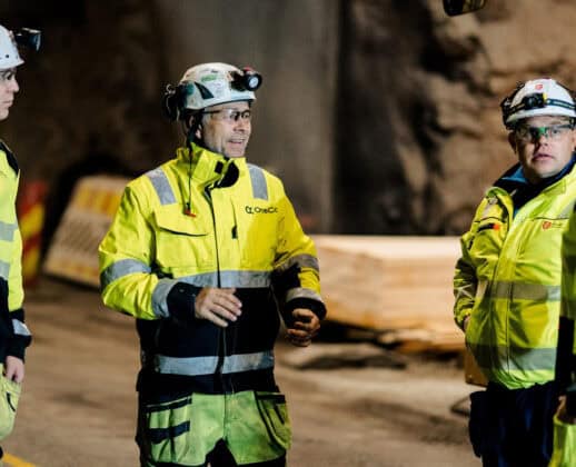 A group of OneCo workers are seen meeting together on the job with helmets and uniforms on.