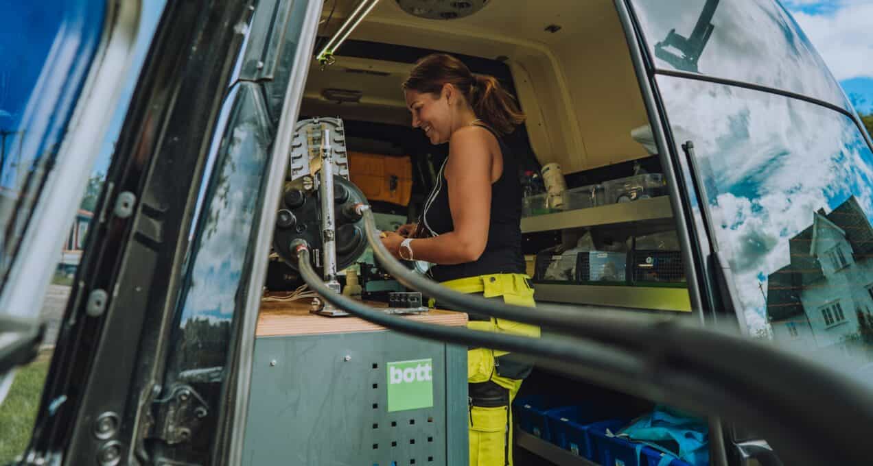 A young worker is seen repairing an item in the back of a work car. The door is open.